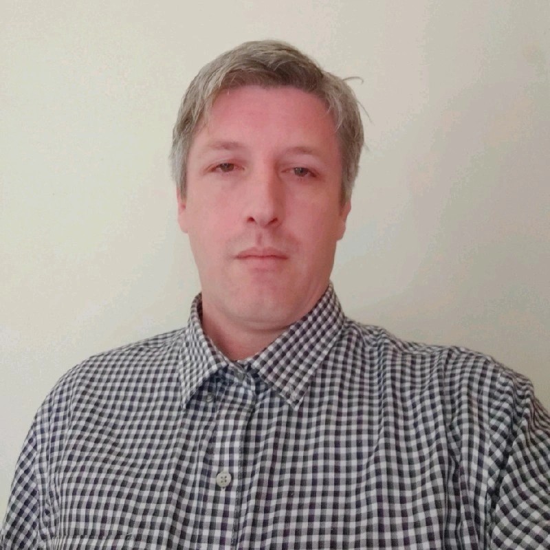 Retrato profesional de una persona sonriente con traje y corbata sobre fondo neutro